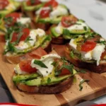 Avocado-Burrata-Bruschetta auf knusprigem Brot, garniert mit frischen Kräutern.