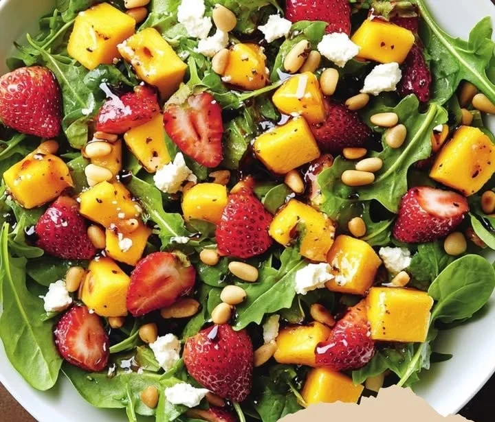 Erdbeer-Mango-Salat mit Spinat, Rucola, Feta und Pinienkernen auf einem Teller