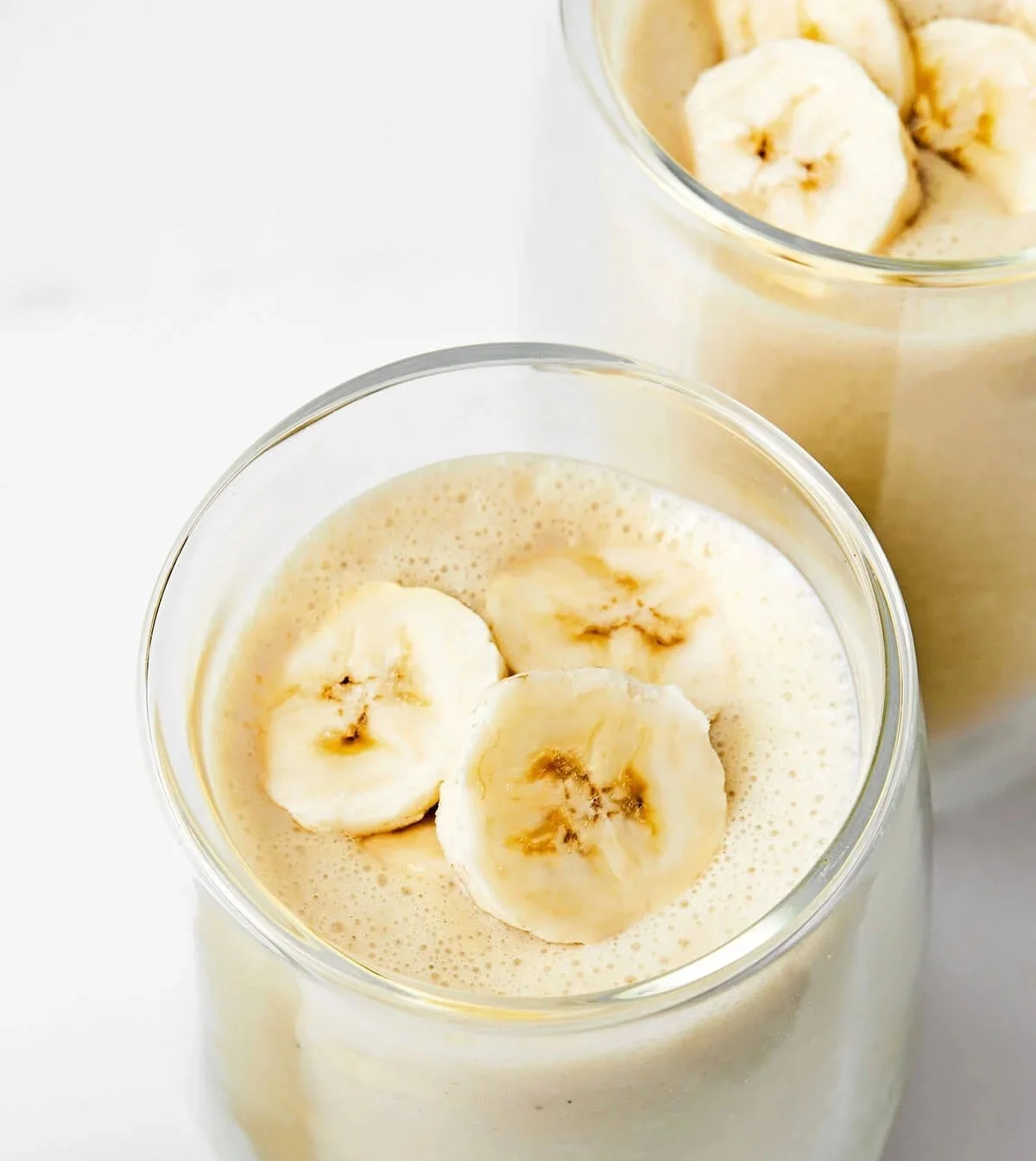 Frischer Bananenshake in einem Glas mit einer Banane daneben.