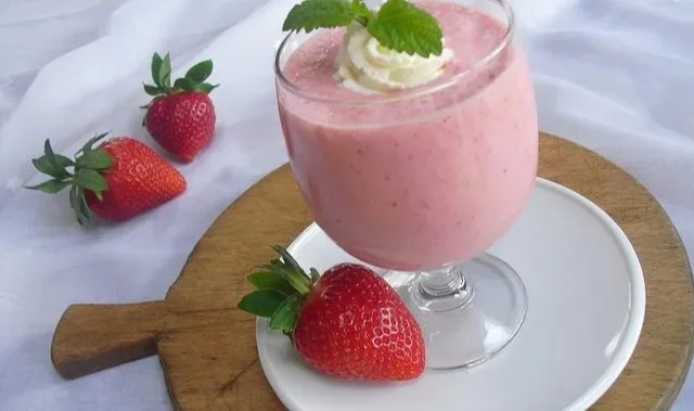Ein erfrischender Erdbeersmoothie in einem Glas mit frischen Erdbeeren.