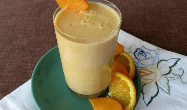 Leckeres Kaki-Orange-Smoothie in einem Glas mit frischen Früchten