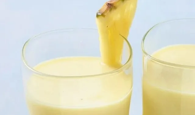 Erfrischender Kokosnuss-Ananas-Smoothie in einem Glas mit Ananasstücken und Kokosraspeln.