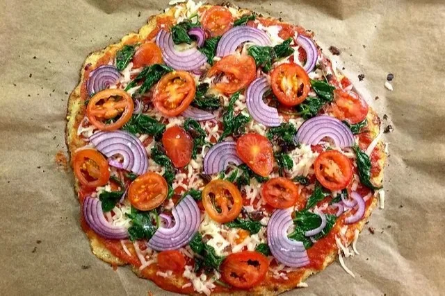 Gesunde Pizza mit Blumenkohlboden auf einem Holzbrett serviert