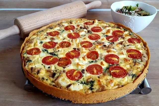 Quiche mit Spinat, Feta, Tomaten und Pinienkernen auf einem Teller