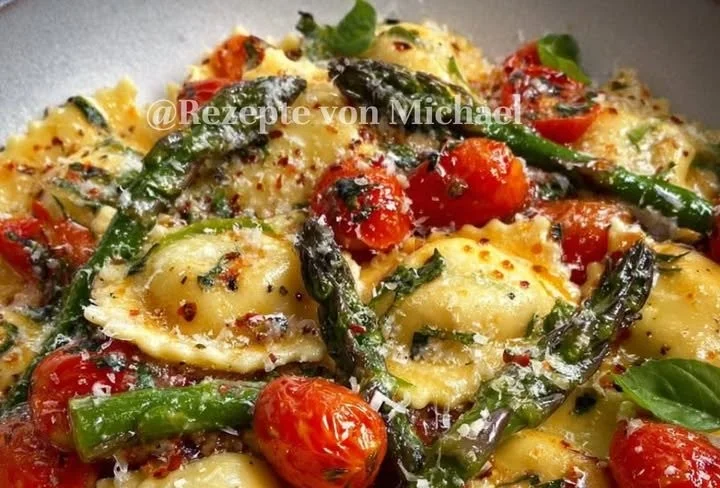 Ravioli mit Tomaten, Spargel, Knoblauch und frischen Kräutern serviert.