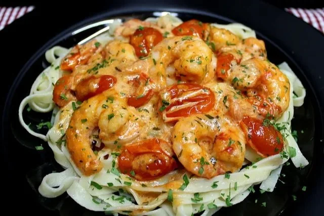 Schüssel mit Shrimp-Tomaten-Cremesauce, serviert mit frischen Kräutern.
