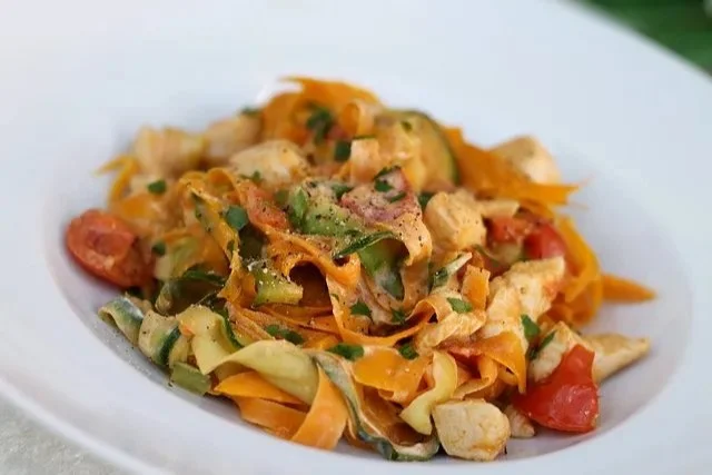 Zucchini-Carotten-Tagliatelle mit Hühnchen und Tomate auf einem Teller