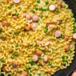 Cremige Nudelpfanne mit Wiener Würstchen und Schmelzkäse auf einem Teller.