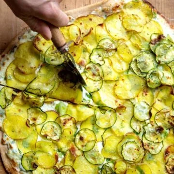 Leckere Kartoffel-Pizza mit Zucchini auf einem Holzbrett.