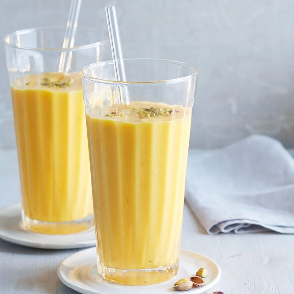 Erfrischendes Mango-Kardamom-Lassi in einem Glas, garniert mit frischen Mangostücken.
