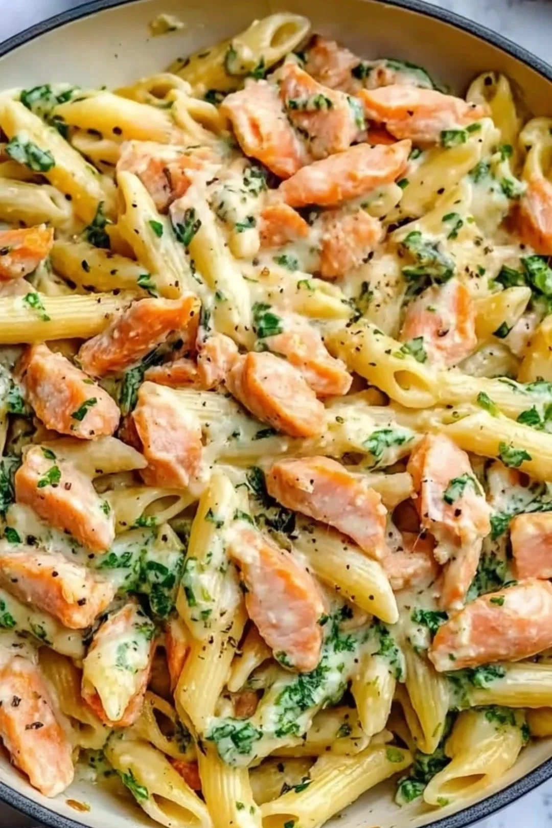 Penne mit Lachs-Cremesauce und frischem Spinat auf einem Teller.
