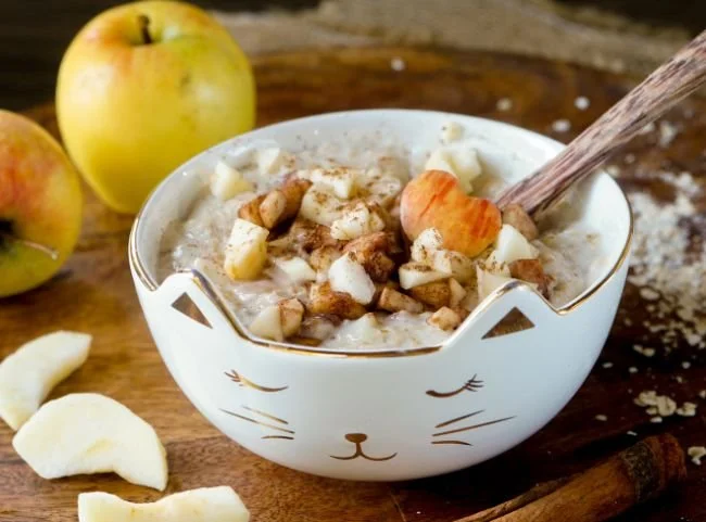 Schüssel Apfel-Zimt-Porridge mit frischen Äpfeln und Zimtstangen