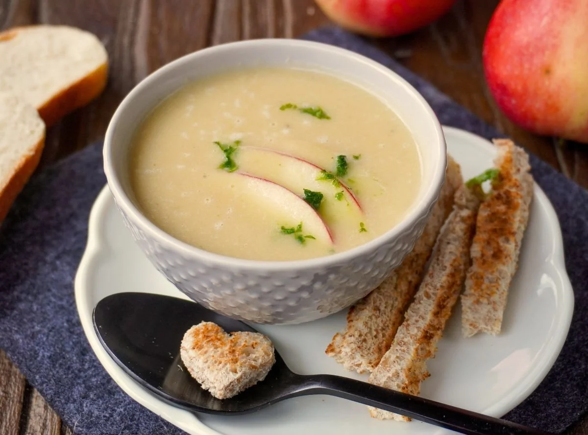 Fruity celery soup with apple served in a bowl, garnished with fresh herbs.