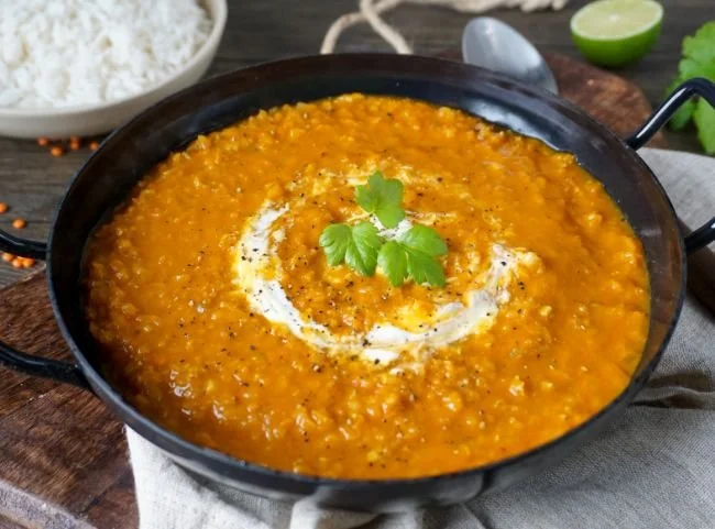 Schüssel mit Rotes Linsen-Dal, garniert mit frischen Kräutern und Gewürzen.