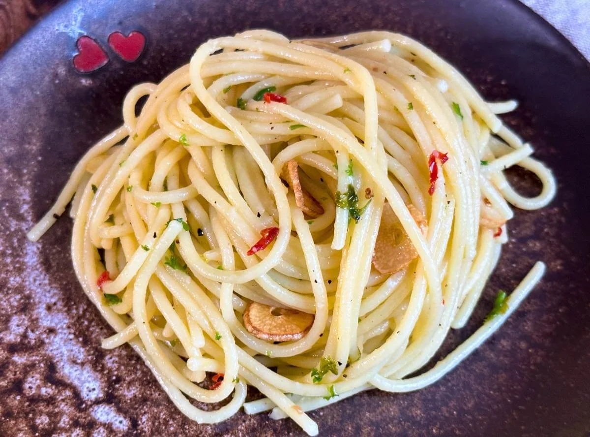 Teller mit Spaghetti aglio e olio und Peperoncino auf einem Holztisch